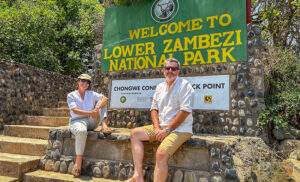 Equipo de Viajes África frente al cartel de entrada al Parque Nacional Lower Zambezi en Zambia, expertos en safaris a medida.