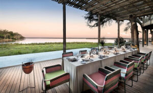 Vista exterior de Lolebezi Lodge entre árboles, con elefante junto al río Zambezi, Lower Zambezi, Zambia