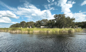 Alojamiento de safari junto al agua en Botswana, rodeado de vegetación y cielo abierto en África.