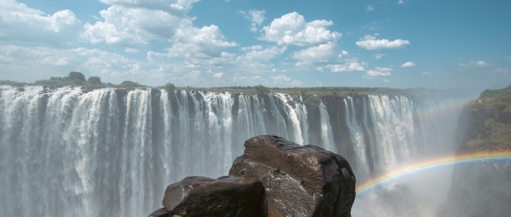 Cataratas Victoria con un arcoíris entre la bruma y rocas en primer plan