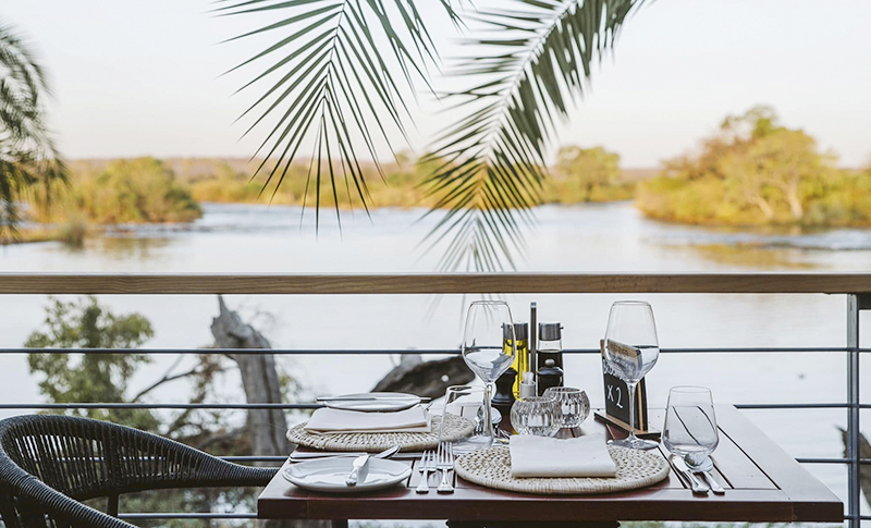 Mesa para dos en Baines Restaurant, con copas y platos preparados frente al río Zambeze.