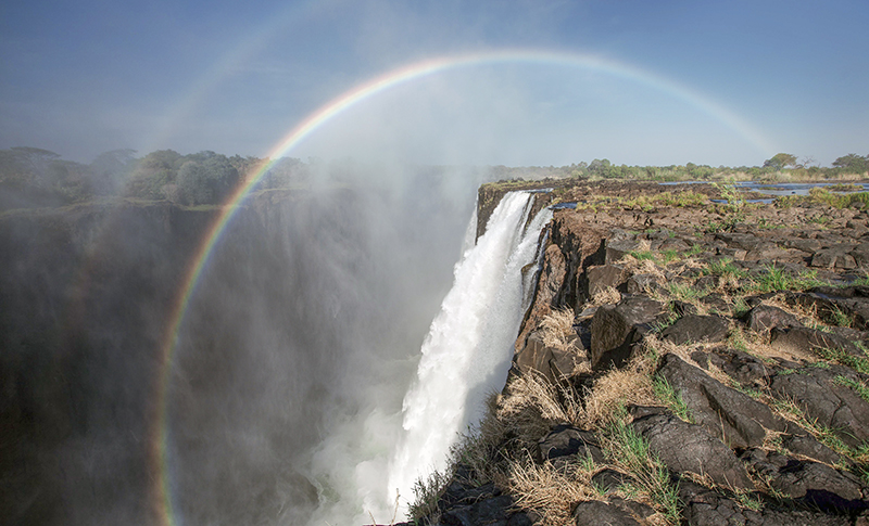 Cataratas Victoria desde el lado de Zambia, con un arcoíris sobre la garganta y bruma junto al salto de agua.