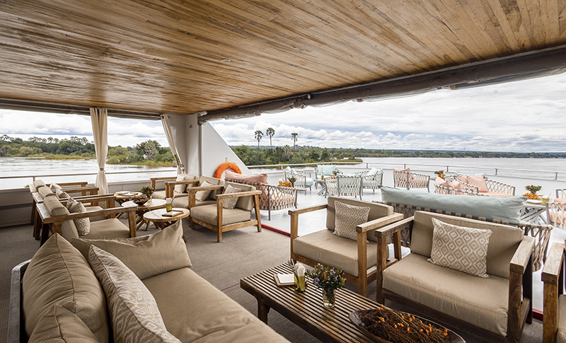 Sofás y butacas en la Signature Deck del Zambezi Explorer, con vistas al río Zambeze.